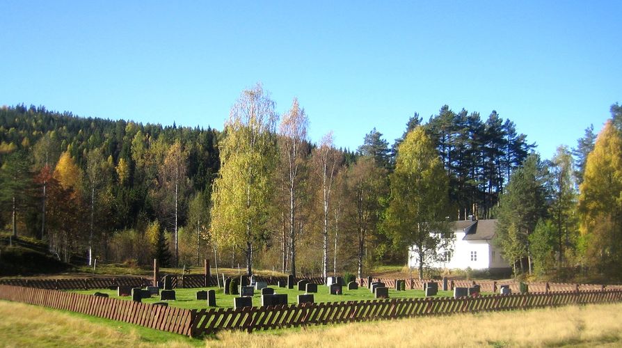 Luksefjell kirkegård med gravminner og gjerdet rundt. Hus i bakgrunnen