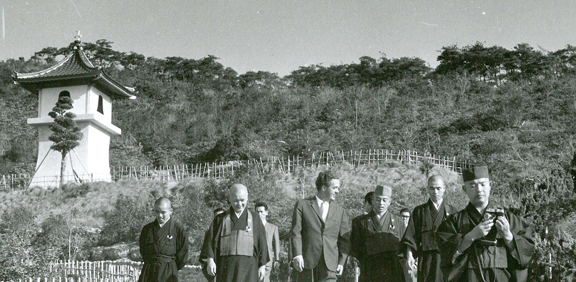 Misjonsprest Harry Thomsen (i midten med dress og slips) foran klokketårnet på Shin Rei San sammen med buddhistprester fra  stedets nabotempler som var invitert til en dagssamling.